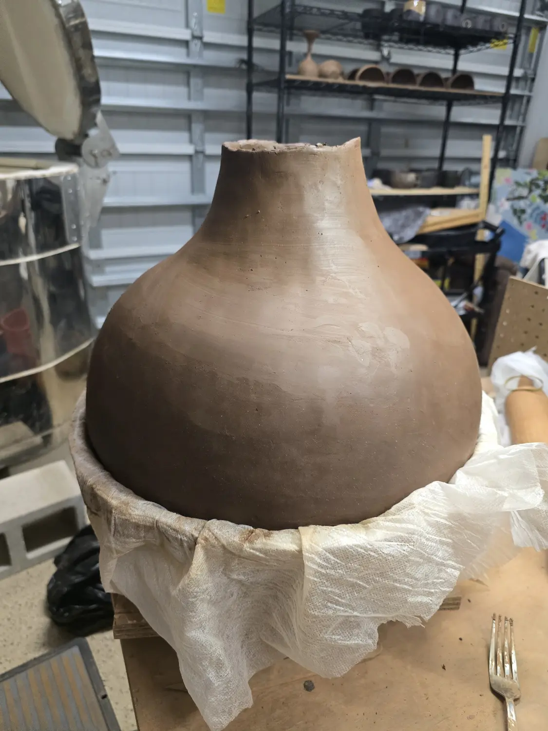 A newly formed clay vessel supported on a studio worktable