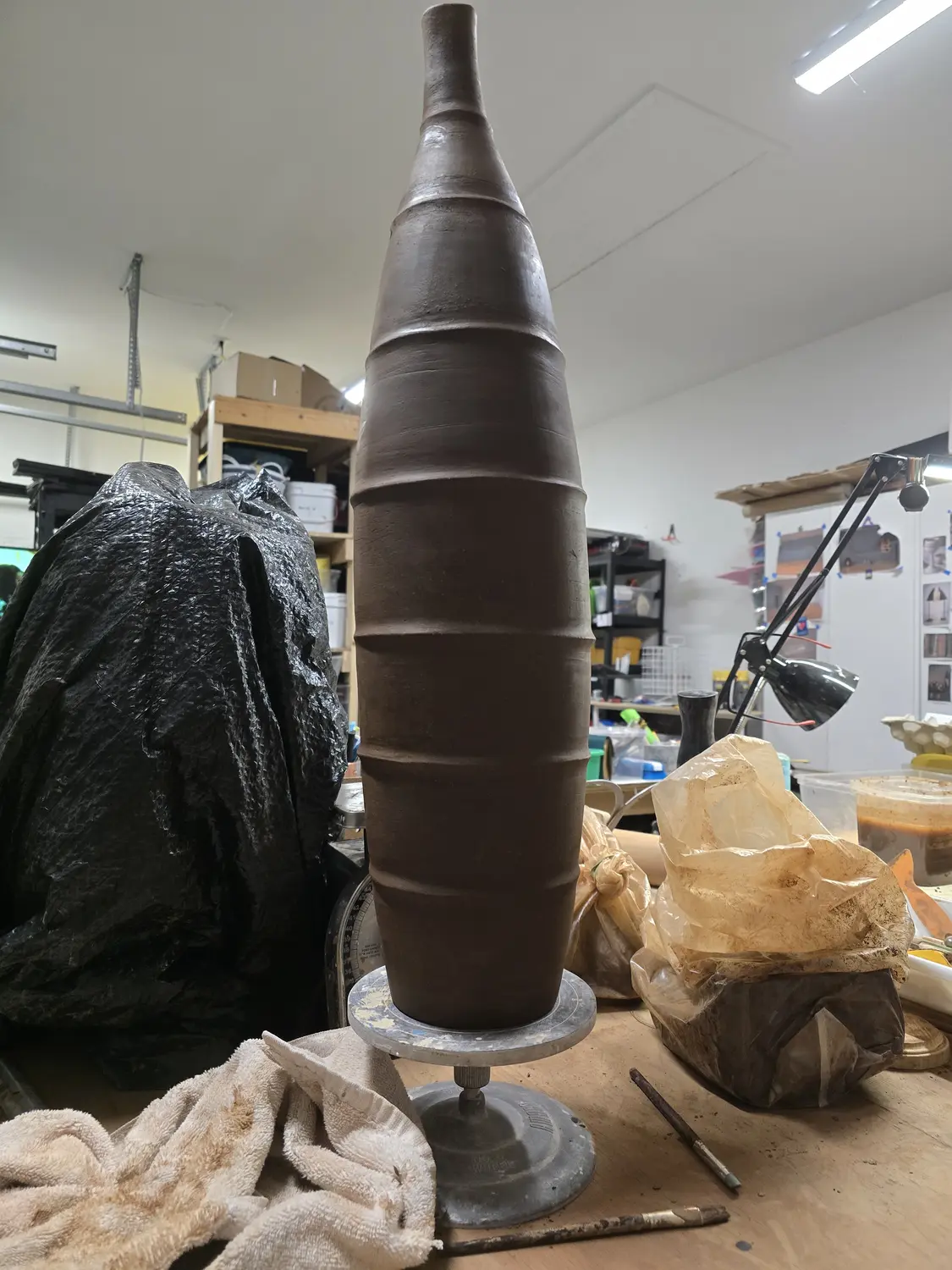 A tall segmented clay vessel on a wheel