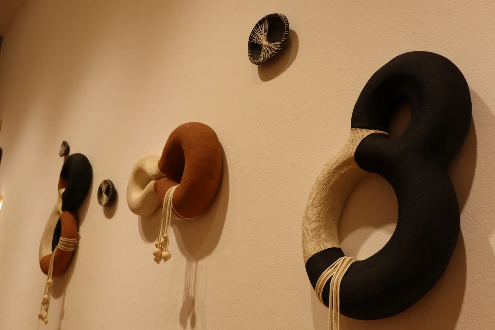 Wall arrangement of black, brown, and white looped ceramic sculptures with hanging thread