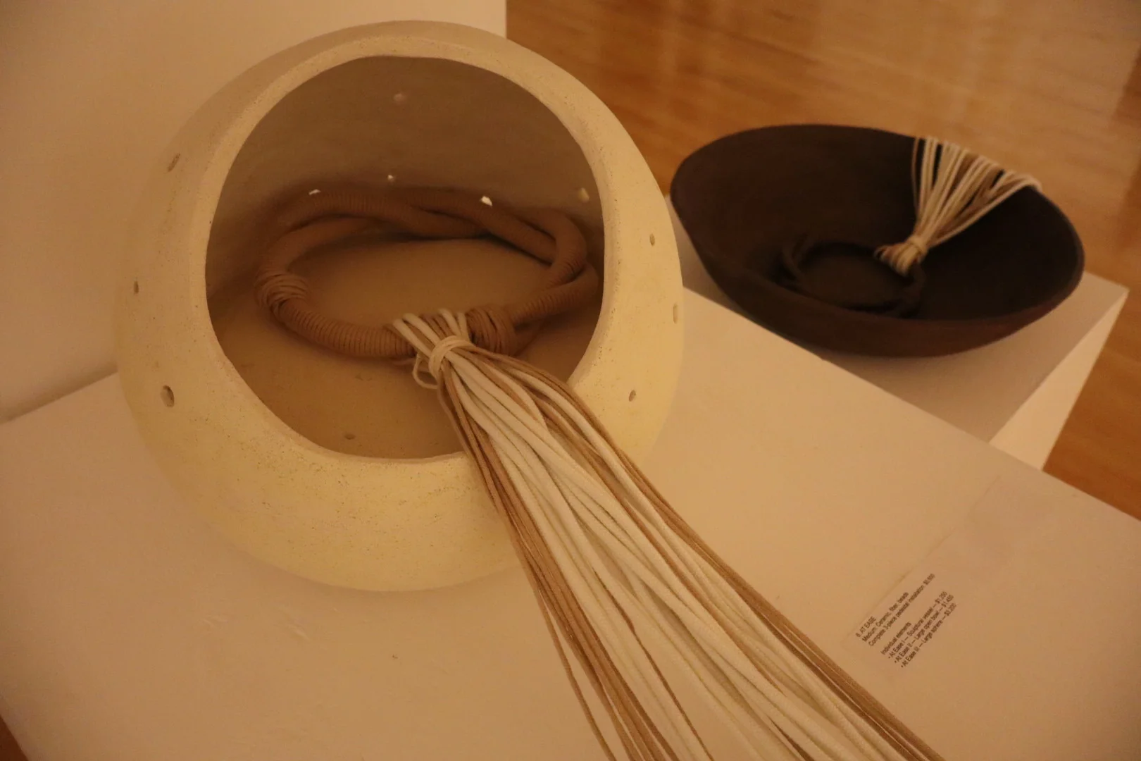 Speckled ceramic bowl with cascading thread and wooden beads on a pedestal